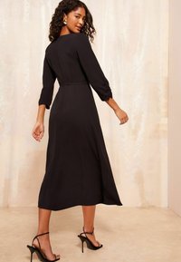 Schwarz midi Kleid mit tailliertem Oberteil, Dreiviertelärmeln und geraffter Taille. Glatter Stoff mit einem subtilen Glanz und ausladendem Saum.