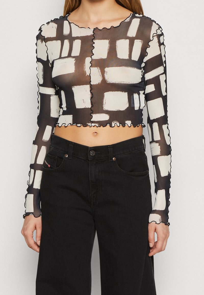 Mustat läpinäkyvät pitkät hihat crop-top, jossa on valkoinen abstrakti siveltimenveto-kuvio ja aaltoilevat reunat. Yhdistetty korkeavyötäröisten mustien farkkujen kanssa.