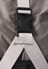 Gray fabric with a checkered pattern features a black plastic buckle and white straps, showing detailed stitching and textile texture.