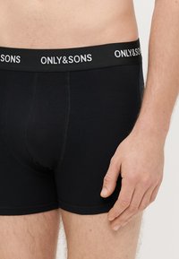 Mustad bokserid pehmest kangast, millel on paks vöökoht, millel on valge "ONLY&SONS" logo, flatlock õmblused ja mugav istuvus.