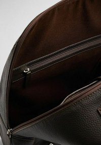 Inredningen av den bruna läderväskan har en slät textur, ett fack med dragkedja och en mörk foder med synliga sömdetaljer.