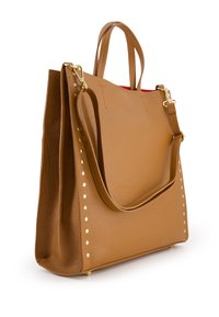 Sac fourre-tout en cuir tan avec des accents en studs dorés, des poignées doubles et une bandoulière amovible. Présente une forme structurée et un intérieur rouge.