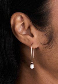 Boucle d'oreille en argent en forme de cercle avec une chute verticale mettant en valeur une seule perle blanche. Le design est épuré, avec une finition lisse et polie.