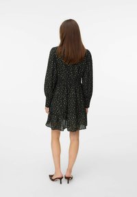 Zwart bloemenjurk met lange pofmouwen, een geraffineerde taille en een gelaagde rok. De achterkant heeft een doorschijnende overlay met kleine bloemmotieven.