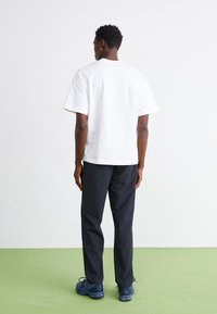 Hvid bomulds T-shirt med korte ærmer, parret med sorte bukser og marineblå sko, set fra baggrunden mod en lys baggrund.