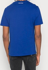 Niebieska bawełniana koszulka z krótkim rękawem, okrągłym dekoltem i małym logo na karku. Prosty dół i luźny krój.