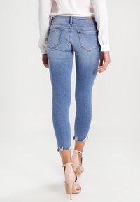 Jeans skinny de denim azul claro con cintura alta, dobladillo deshilachado y dos bolsillos traseros, combinados con sandalias de tacón alto beige.