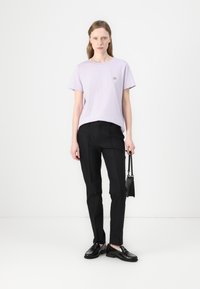 Lyse lilla bomulls t-skjorte med korte ermer og en liten logo. Svarte skreddersydde bukser med slim fit og svarte loafers. Minimalistisk design.