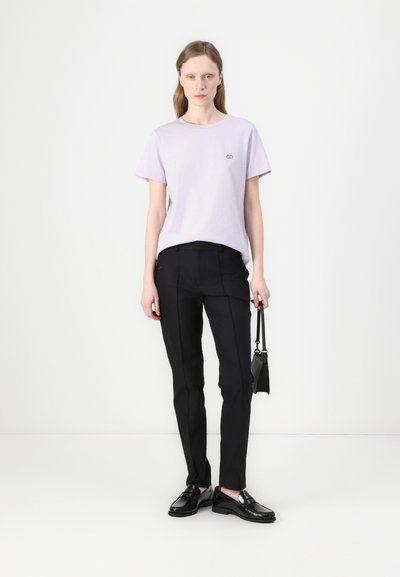 T-shirt en coton violet clair avec des manches courtes et un petit logo. Pantalon noir taillé avec une coupe slim, et mocassins noirs. Design minimaliste.