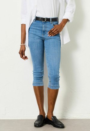 Hele sinised lõhikutega teksapüksid, millel on istuv lõige, ülesrullitud äärikud ja kõrge vöökoht, kombineeritud musta nahkvöö ja mustade libisevate kingadega.