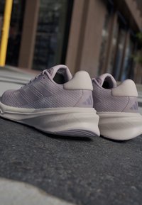 Zapatillas deportivas moradas con parte superior texturizada, tres franjas laterales y suela de goma. Cuenta con un collar acolchado y acentos en el talón de color contrastante.