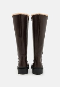 Bottes en cuir marron à hauteur de genou avec une douce fourrure au sommet, fermeture éclair sur le côté intérieur et semelles en caoutchouc texturé.