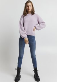 Hellblauer Strickpullover mit geripptem Muster und Ballonärmeln, kombiniert mit enganliegenden blauen Jeans und schwarzen Schnürstiefeln im Combat-Stil.