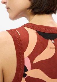 Červený top bez rukávů s abstraktními květinovými vzory v odstínech růžové, oranžové a černé. Hladká textura s kontrastním prošitím podél výstřihu.