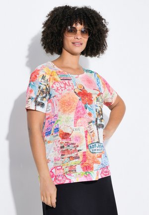 Colorful short-sleeve t-shirt featuring a collage of various printed labels and graphics in hues of pink, red, blue, and yellow.