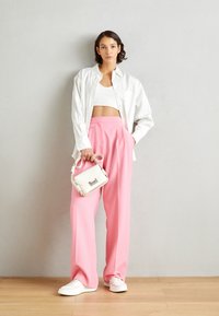 Camisa blanca de gran tamaño, top blanco cortado y pantalones anchos rosa, combinados con un pequeño bolso blanco y zapatillas blancas sobre el suelo de madera.