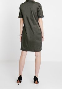 Sukienka z krótkim rękawem w ciemnozielonym kolorze z kołnierzykiem. Gładki materiał, długość do kolan, kieszenie wszyte w boczne szwy. Noszona z czarnymi szpilkami.