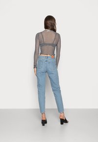 Top de malla a rayas en blanco y negro con mangas largas y dobladillo festoneado, combinado con jeans de mezclilla de tiro alto en azul claro y tacones gruesos negros.