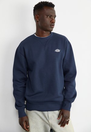Sudadera azul marino con cuello de barco y puños acanalados, que presenta un pequeño logo bordado en el pecho y un corte holgado.