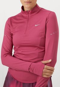 Langarm, rits-atletiekshirt in levendig roze. Gemaakt van gladde stof, met reflecterend logo en duimopeningen op de mouwen voor extra comfort.