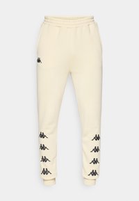 Crème-kleurige trainingsbroek met zwarte Kappa-logo's langs beide benen en een elastische tailleband met trekkoord.