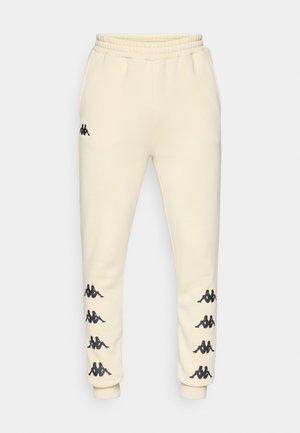 Crème-kleurige trainingsbroek met zwarte Kappa-logo's langs beide benen en een elastische tailleband met trekkoord.
