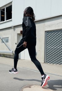 Haut de sport noir avec des lignes d'accentuation blanches, associé à un legging noir. Comprend des chaussures de course avec une tige noire et une semelle rouge.