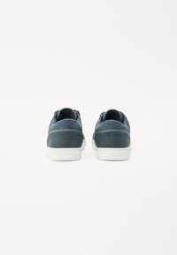 Sapatilhas azul-escuro com detalhes em tecido texturizado, solas brancas de borracha planas e um design simples, apresentando um corte baixo e atacadores nas costas.