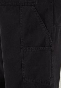 Gros plan d'une poche de pantalon en tissu noir avec des coutures visibles et des détails de couture.