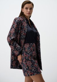 Ensemble blazer et jupe à motif marine, présentant des designs floraux en rouge, rose et blanc. Tissu lisse avec une coupe structurée et des manches longues.