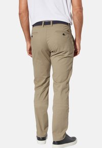Beige cotton pants with a straight fit, featuring two back pockets and a textured navy belt, worn with black sneakers.