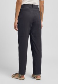 Schwarze, leichte Hosen mit einem entspannten Schnitt, hoch geschnitten und mit zwei Abschnitten an den Beinen, kombiniert mit sandalen mit offenen Zehen.