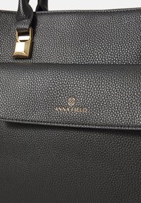 Black textured leather handbag with gold clasp and Anna Field brand logo centered on front flap.