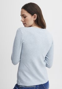 Gaiši zils garās piedurknes džemperis ar apaļu kakla izgriezumu. Mīksta, adīta tekstūra. Iespējota brīva piegriezuma un sānu šķēlumi apakšmalā.