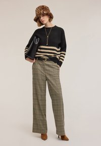 Maglione a righe nero e crema, pantaloni larghi a quadri verdi, cappello a secchiello con stampa leopardata, borsa nera e décolleté marroni a punta.