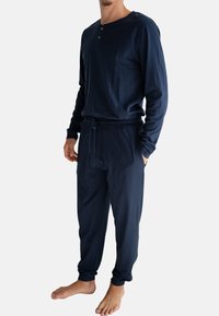 Maglia blu navy a maniche lunghe con colletto henley e dettagli con bottoni abbinata a pantaloni con cordino coordinati. Tessuto leggero e morbido.