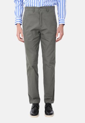 Pantaloni in cotone verde oliva con una vestibilità slim, design a cinque tasche e chiusura con bottone. Indossati con scarpe nere.