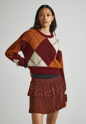 Suéter de punto con un diseño de argyle en burdeos, naranja y crema. Combinado con una falda roja de textura plisada.