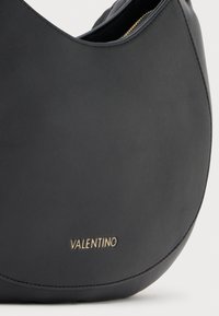 Μαύρη δερμάτινη τσάντα χειρός με καμπύλη σχήμα. Διαθέτει χρυσό λογότυπο "VALENTINO" και λεπτή, λεία υφή. Ορατό φερμουάρ για άνοιγμα.