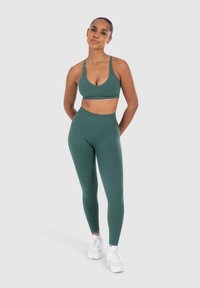Reggiseno sportivo verde e leggings a vita alta realizzati in tessuto morbido e elasticizzato. Presentano un design semplice e una silhouette aderente.
