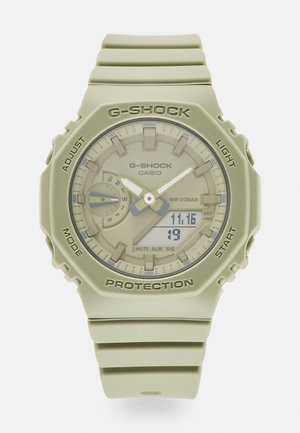 Montre Casio G-Shock beige avec affichage analogique et numérique, affichant la date et l'heure, avec des boutons étiquetés pour régler, mode, lumière et démarrer.
