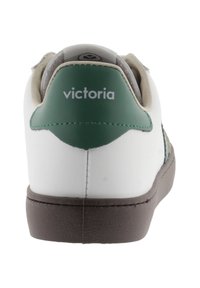 Sneaker blanche avec des accents verts, semelle marron, panneau arrière texturé et logo "victoria". Matériau lisse avec des détails cousus.