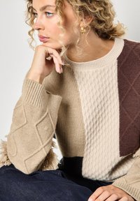 Maglione patchwork beige e marrone con texture a coste e a treccia, dotato di scollatura rotonda e finiture frangiate all'orlo.