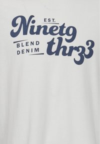 Hvid bomulds T-shirt med marineblå grafisk tekst: "ETABLERT. Treoghalvfjerds Blend Denim." Enkel design uden yderligere mønstre eller accenter.