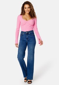 Top lungo a maniche con costine rosa e scollatura a barca, abbinato a jeans flare in denim blu a vita alta. Tacchi aperti neri.
