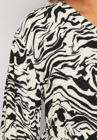 Black and white dress featuring a zebra stripe pattern, made of textured fabric with a v-neck design and long sleeves.