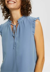 Light blue blouse with ruffled sleeves, a keyhole neckline, and a tie closure. The fabric is smooth and flows gently.