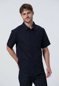 Chemise à manches courtes bleu marine avec un col, dotée d'une poche poitrine, d'une texture subtile et d'un tissu lisse. Portée avec un jeans foncé.