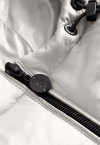 Lichtgrijs geïsoleerd jacket materiaal met een zwarte rits, voorzien van een cirkelvormige zwarte ritskoord met een hondenlogo en rode accenten.