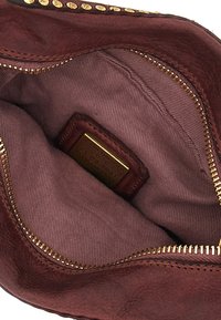 Interno di una borsa in pelle bordeaux con texture liscia, zip dorata e fodera in tessuto. È visibile un'etichetta con testo impresso su un lato.